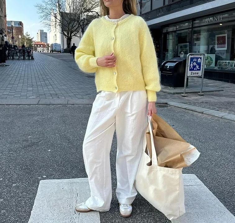 Cardigan doux look clean girl jaune porté par une femme avec pantalon blanc et sac beige