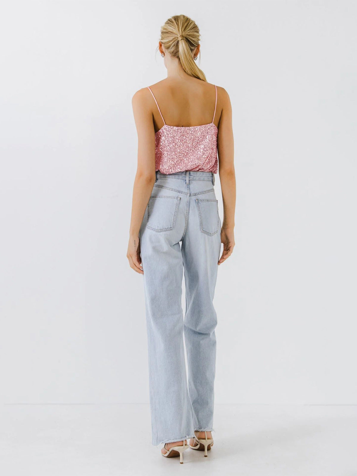 Femme de dos portant un débardeur sequin tendance 2024 rose avec jeans larges et sandales