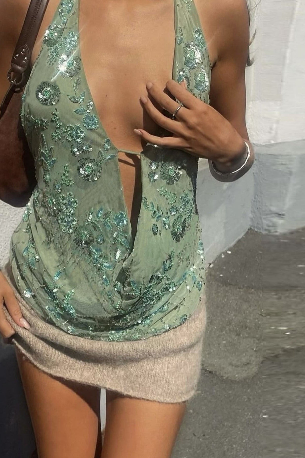 Femme portant un haut dos nu vert pastel avec détails pailletés et jupe courte beige