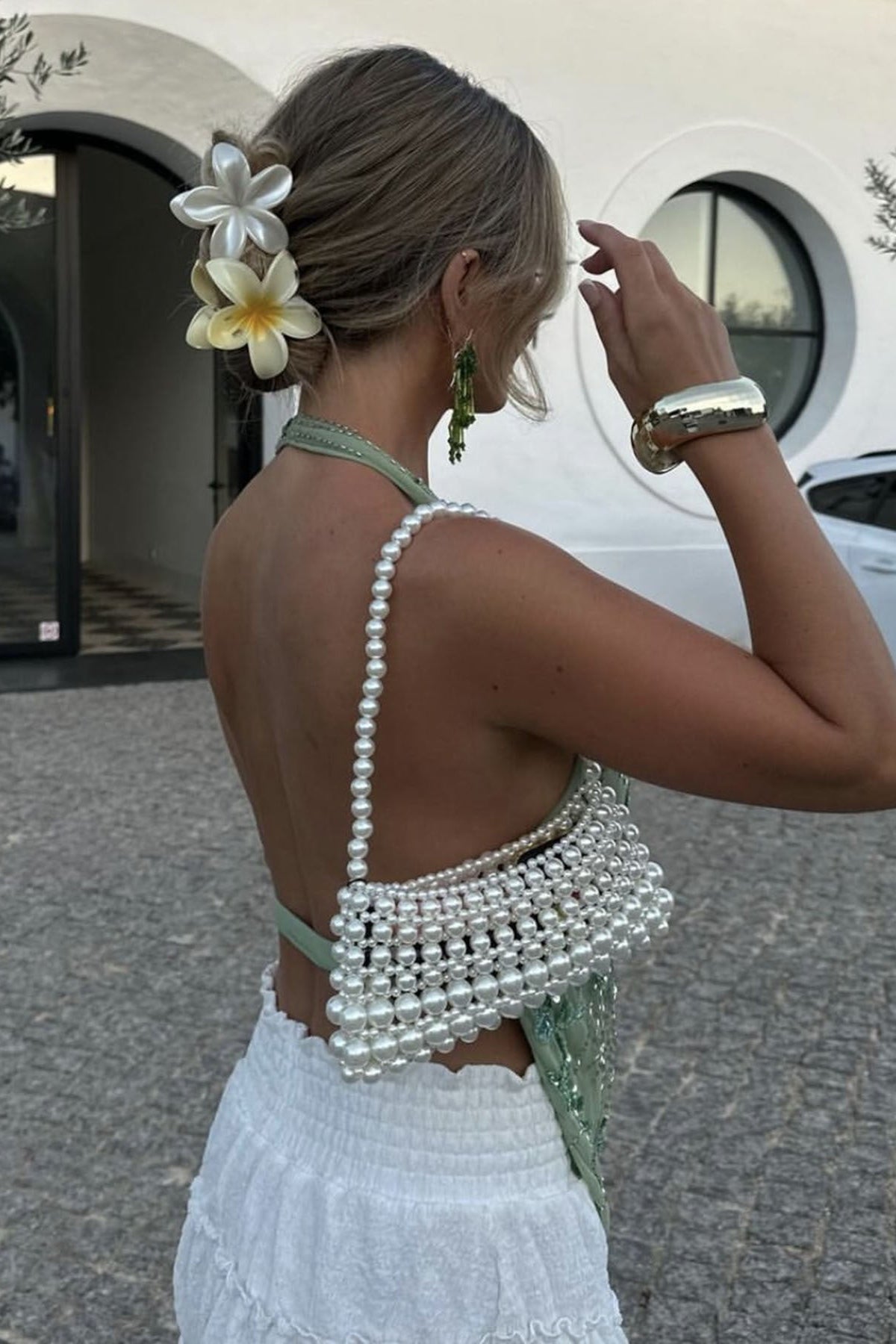Femme portant un haut dos nu vert pastel avec un sac à perles blanches et une jupe blanche