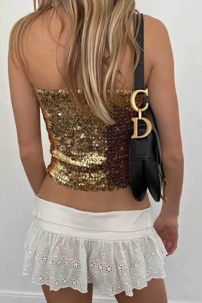 Femme portant un haut style nordique chic doré à sequins et jupe blanche brodée avec sac noir