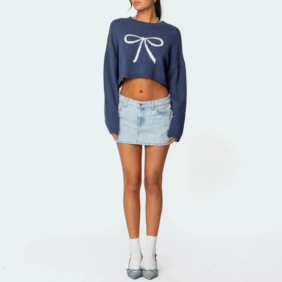 Femme portant un pull bleu avec un nœud blanc et une jupe courte jean scandinave claire