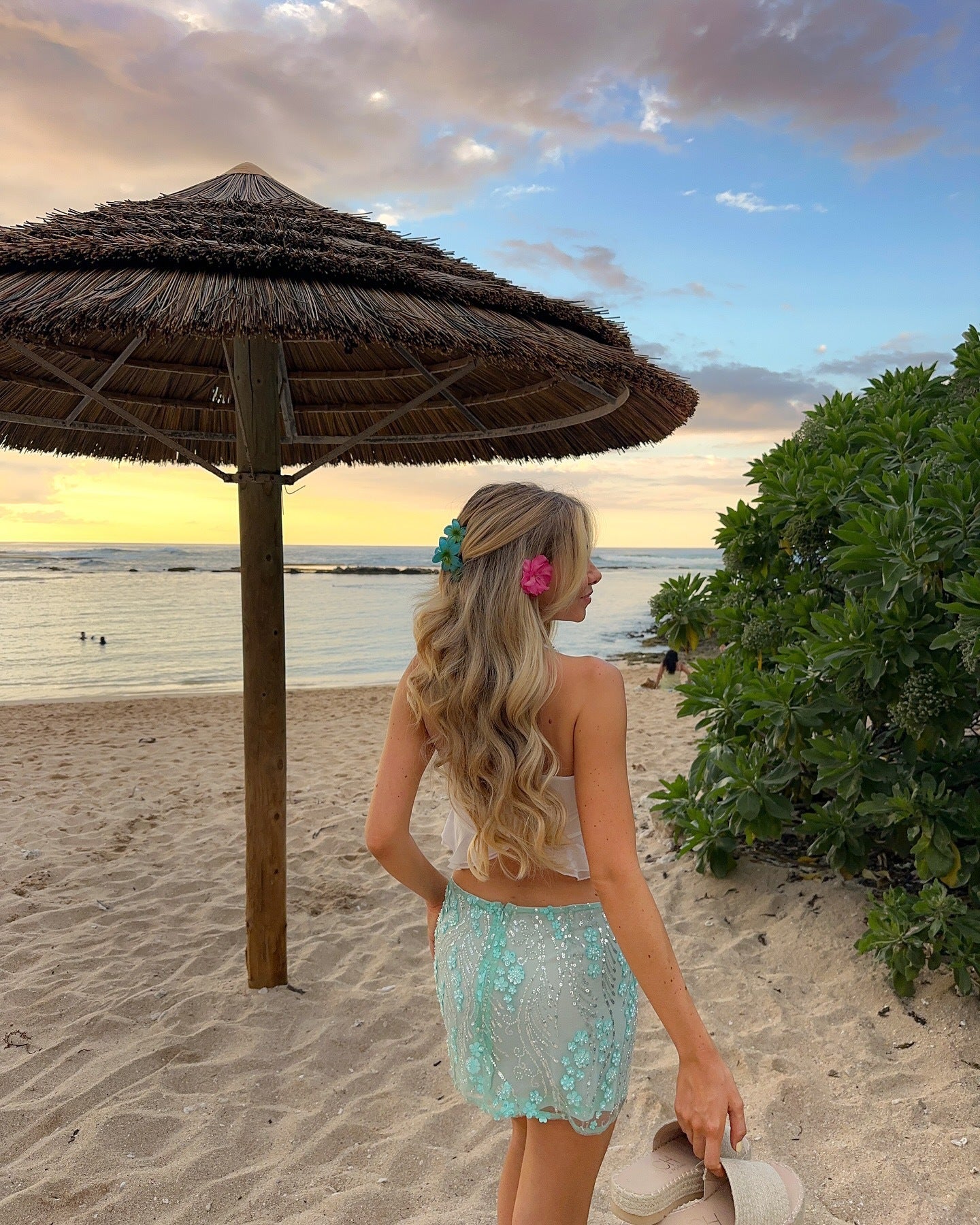 Femme portant un top blanc et une jupe style Stockholm soirée turquoise transparente au bord de la plage au coucher du soleil