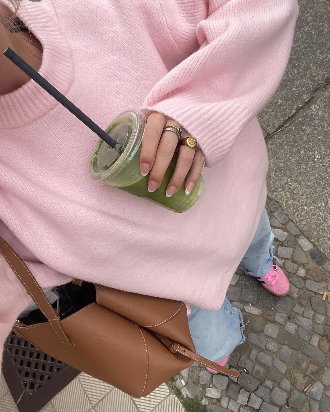 Femme portant un look clean girl cardigan rose avec un sac marron et un jus vert à emporter