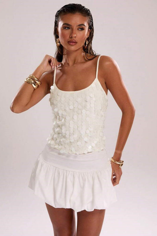 Top blanc à fines bretelles style look clean girl nordique porté par une femme avec jupe blanche