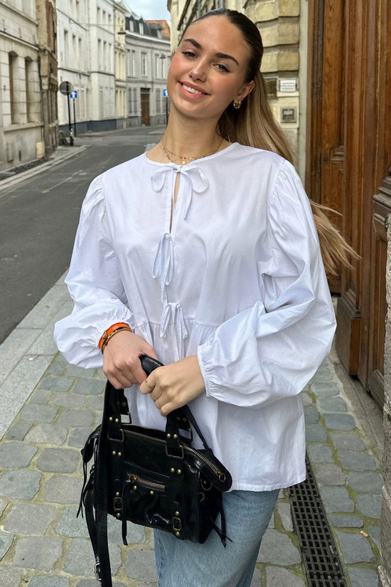 Haut scandinave femme tendance blanc à manches bouffantes porté avec un sac noir élégant