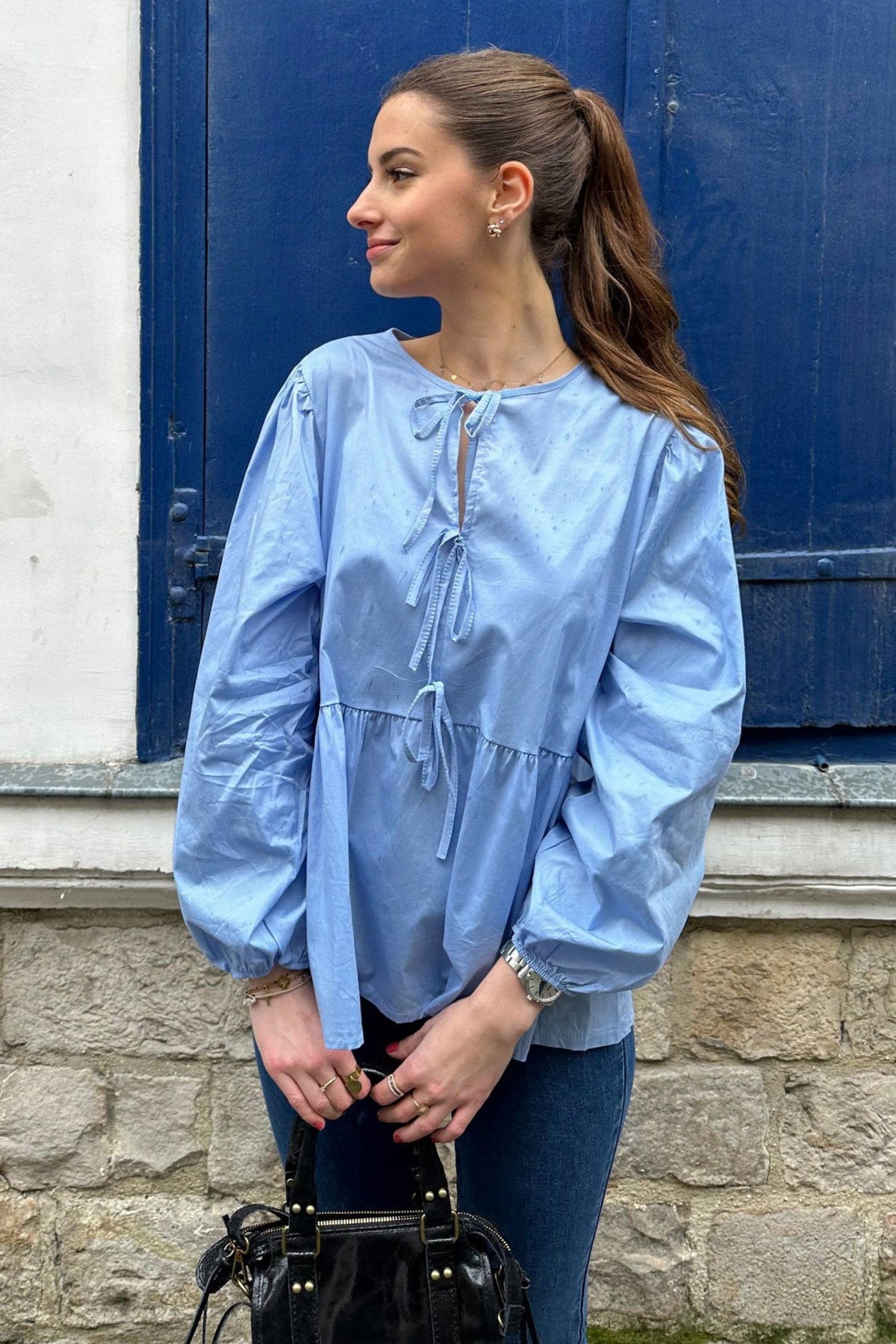 Haut scandinave femme tendance bleu clair à manches bouffantes et détails à nouer porté avec un sac noir