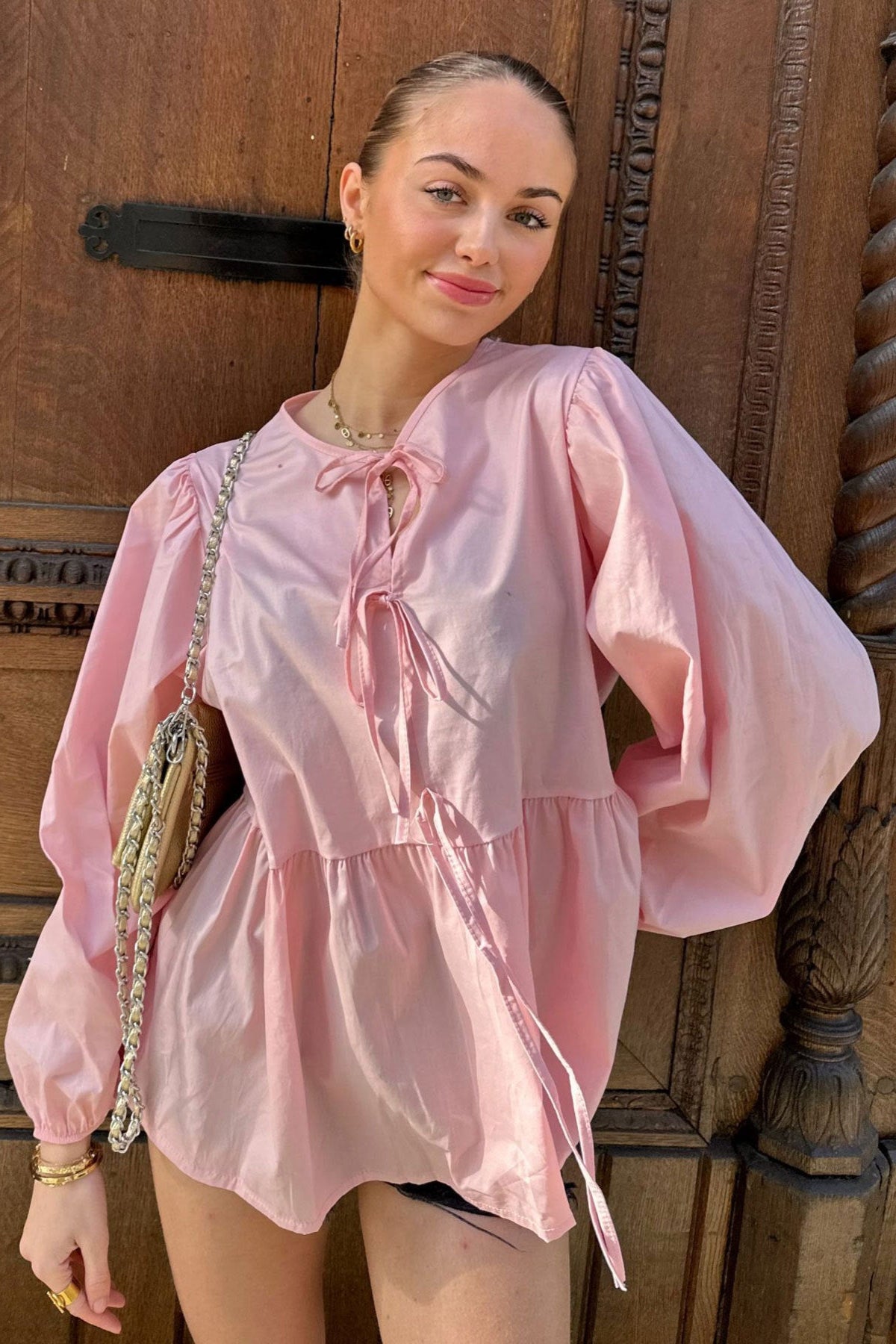 Haut scandinave femme tendance rose à manches bouffantes porté par une femme devant une porte en bois