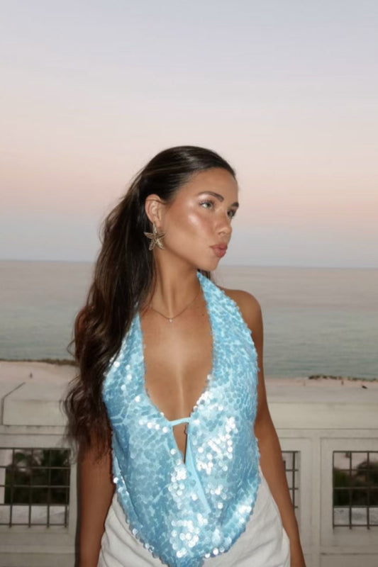 Femme portant un haut à sequins bleu femme à col plongeant sur fond de mer au coucher du soleil