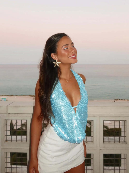 Femme portant un haut à sequins bleu femme My Store avec décolleté plongeant sur fond de bord de mer