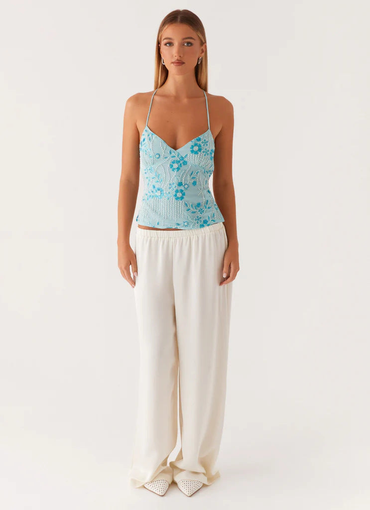 Femme portant un haut bleu style ibiza à fines bretelles avec pantalon blanc fluide