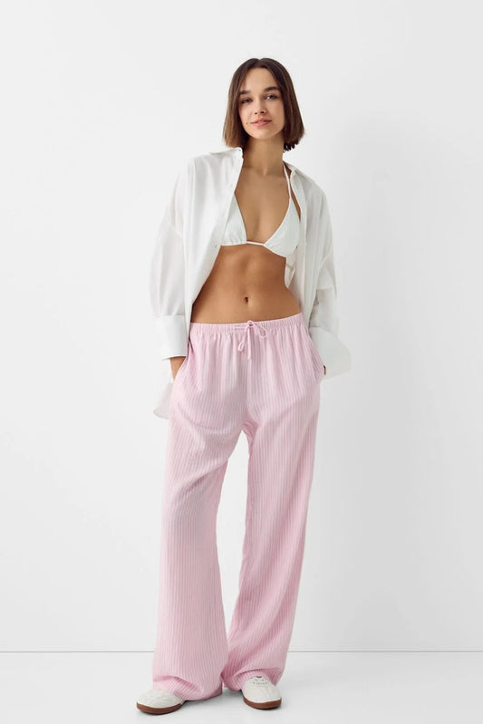 Femme portant un pantalon scandinave style clean girl stockholm style rose avec un top blanc et une chemise ouverte