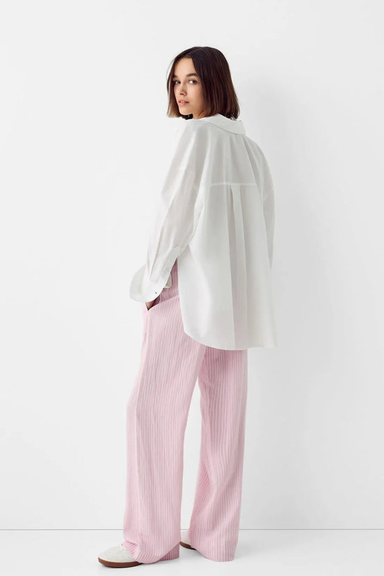 Femme portant un pantalon scandinave style clean girl stockholm style rose avec un haut blanc fluide