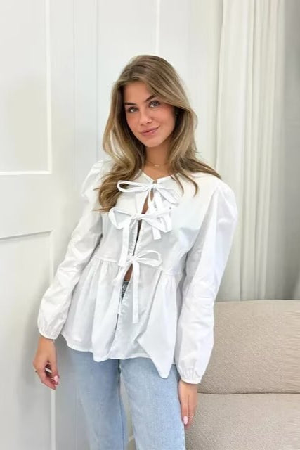 Top blanc clean girl tendance à manches longues avec nœuds devant porté par une femme blonde